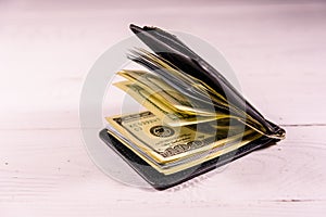 Black leather money clip with the one hundred dollar bills on wooden table