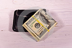 Black leather money clip with the one hundred dollar bills on wooden table