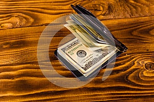 Black leather money clip with the one hundred dollar bills on wooden table