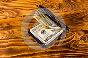 Black leather money clip with the one hundred dollar bills on wooden table