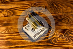 Black leather money clip with the one hundred dollar bills on wooden table