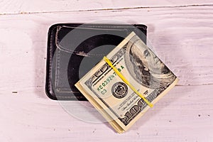 Black leather money clip with the one hundred dollar bills on wooden table. Top view