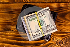 Black leather money clip with the one hundred dollar bills on wooden table. Top view