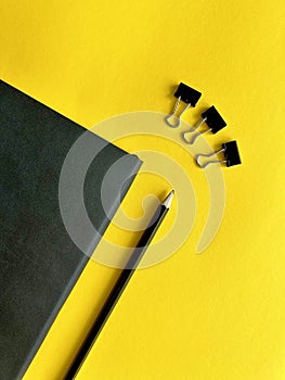 black leather notepad, pencil, paper clips, paper clips on yellow background, business