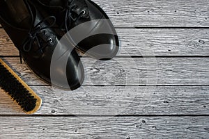 Black leather shoes and brush for cleaning shoes on a gray wooden background. A pair of stylish women`s boots