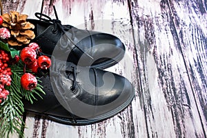 Black leather shoes and Christmas decor on wooden background. Pair of stylish women`s boots and spruce twig with Christmas toys