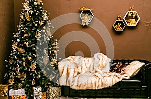 Black leather sofa with fur cape and Christmas tree with gifts in a stylish home interior. New Years decor