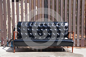 Black leather sofa and wooden armrest chair with brown background.