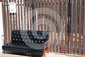 Black leather sofa and wooden armrest chair with white mailbox on brown background.