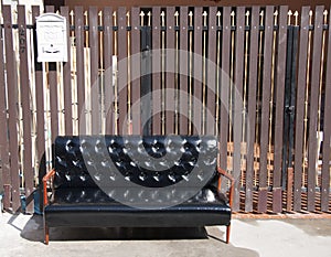 Black leather sofa and wooden armrest chair with white mailbox on brown background.