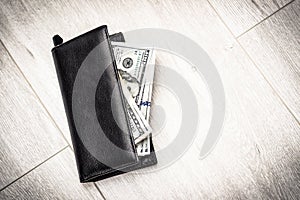 Black leather wallet with american dollars on a gray wooden floor background, close-up with copy space. Full of money. Good