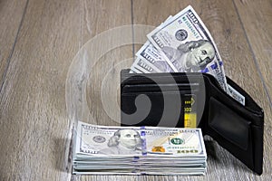 Black leather wallet with dollars and a credit card inside on a gray wooden table