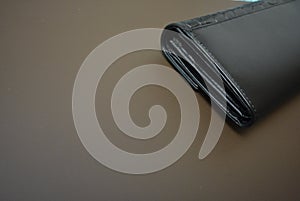 Black leather wallet, genuine cowhide leather women`s wallet located on a matte brown background. Money and finance, saving money