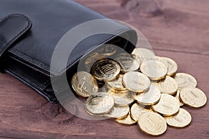 Black leather wallet with golden coins on wood background