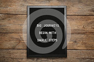 Black letter board with motivational quote Big Journey Begin with Small Steps on wooden background, top view