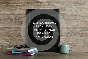 Black letter board with motivational quote a Dream Becomes a Goal When Action is Taken Toward its Achievement, notebooks and cup