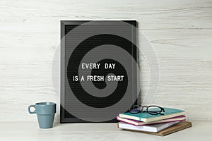 Black letter board with motivational quote Every Day is a Fresh Start, notebooks, glasses and cup on white wooden table