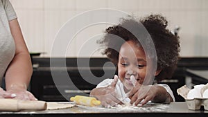 Black little girl with her mother in the kitchen - the girl playing with flour