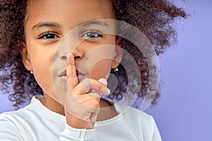 black little girl holding finger on lips symbol of hush gesture of asking to be quiet
