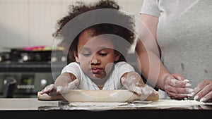 Black little girl rolling out the dough in the bright kitchen