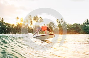 Black long-haired teen boy riding and jumping from a long surfboard. He caught a  wave in an Indian ocean bay with magic sunset