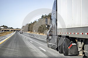 Black long hauler big rig semi truck transporting cargo in dry van semi trailer driving on the straight multiline highway road