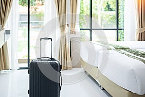 Black Luggage in modern hotel room with windows, curtains and bed against green nature background. Time to travel, relaxation,