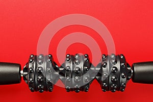 Black lumpy foam body massage roller on red background