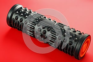 Black lumpy foam massage roller on red background. For the mechanical and reflex effects on tissues and organs