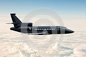 Black luxury executive business jet flies in the air above the clouds