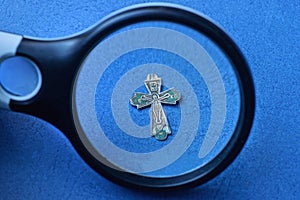 Black magnifier enlarges a small old gray silver cross
