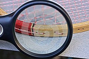 Black magnifier magnifies part of brown wooden badminton racket