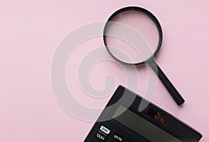 Copy space black magnifying glass and calculator on pink pastel background.Business and finanse concept