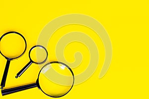 Black magnifying glass on light yellow background with copy space.