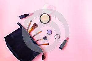 Black makeup bag with cosmetic beauty products and make-up brushes on pink background