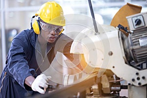 Black male african american workers wear sound proof headphones and yellow helmet working an iron cutting machine in background