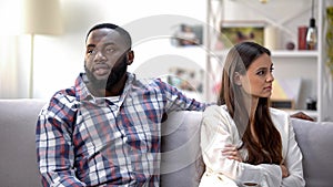 Black male depressed about conflict, sitting on sofa with offended girlfriend