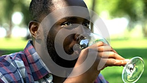Black male drinking wine, gathering with friends in park, relax time on picnic