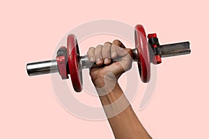 Black male hand holding metal and red dumbbell on pink background.