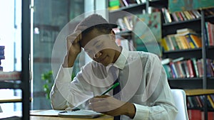 Black male high-schooler thinking about task, doing homework at campus library