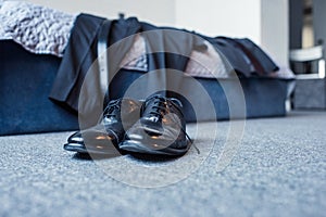 Black male leather shoes on floor in bedroom with business suit placed on bed