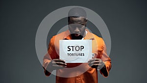 Black male prisoner holding stop tortures sign, ill treatment abuse of force