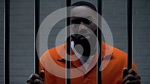 Black male prisoner waiting for sentence in prison cell, looking sadly to camera