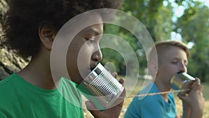 Black male teen listening to tin can phone communicating with friend, kids fun