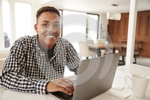 African American  male teenager using a laptop computer at home smiling to camera, close up photo