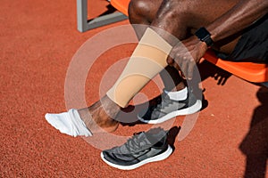 A black male track and field athlete puts compression leggings on his leg before a race at the stadium