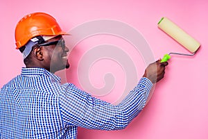 Black man African American holding paint roller in hand paints the wall in pink color .happy african builder painting