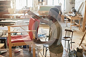 Black man as craftsman refurbishing chair in carpentry workshop