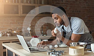 Black man baking pastry and looking recipe in laptop