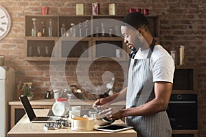 Black man baking pastry with recipe on laptop